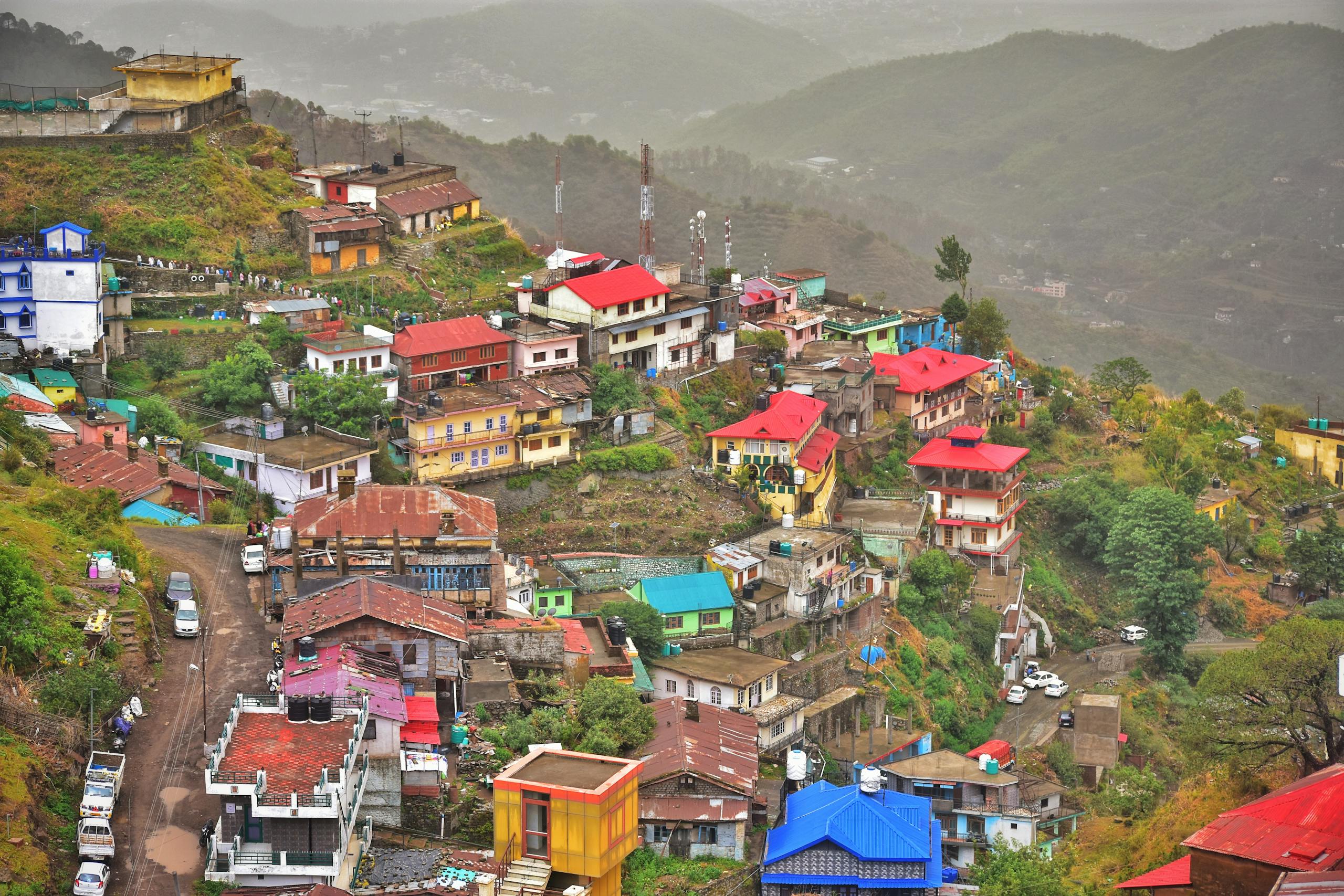 A vibrant aerial view of a colorful hillside town in Shimla with misty mountains.
