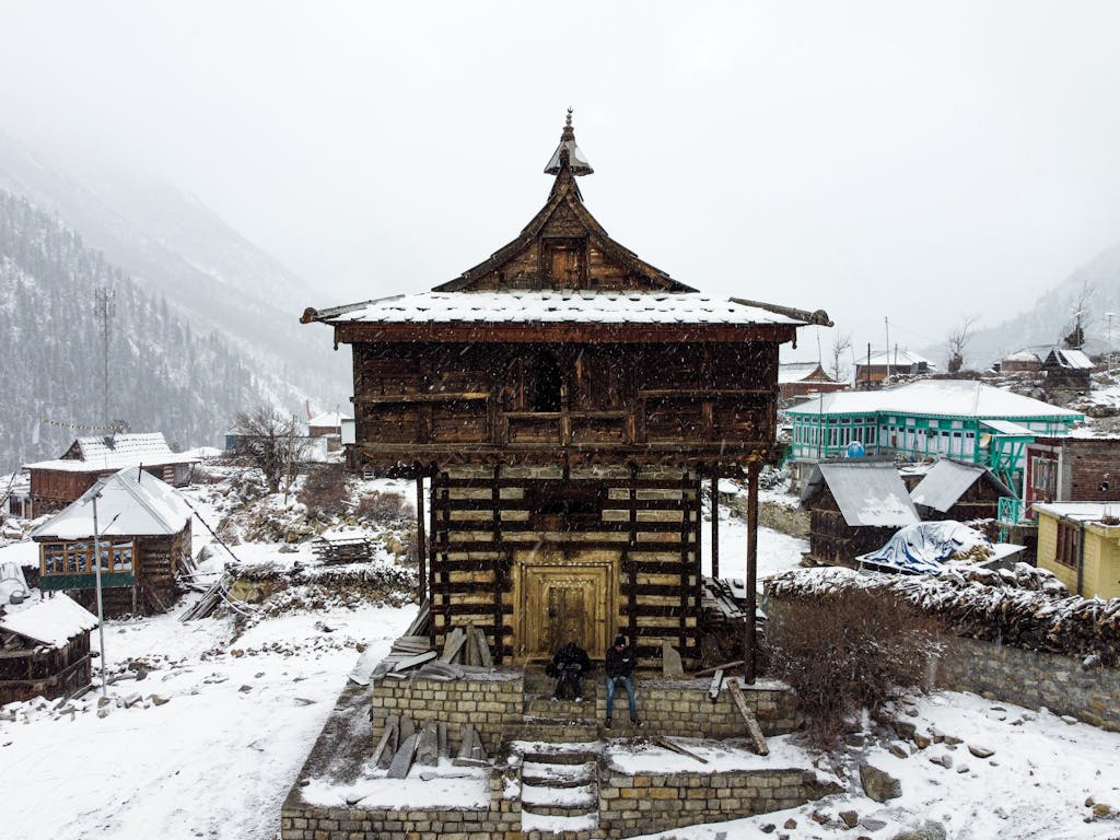Traditional wooden temple in snowy landscape in the Himalayas, showcasing snowfall and rustic architecture.