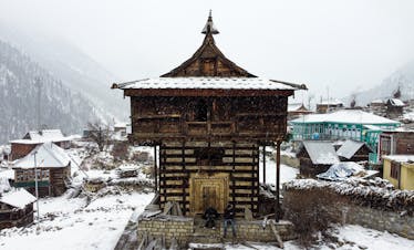 Traditional wooden temple in snowy landscape in the Himalayas, showcasing snowfall and rustic architecture.