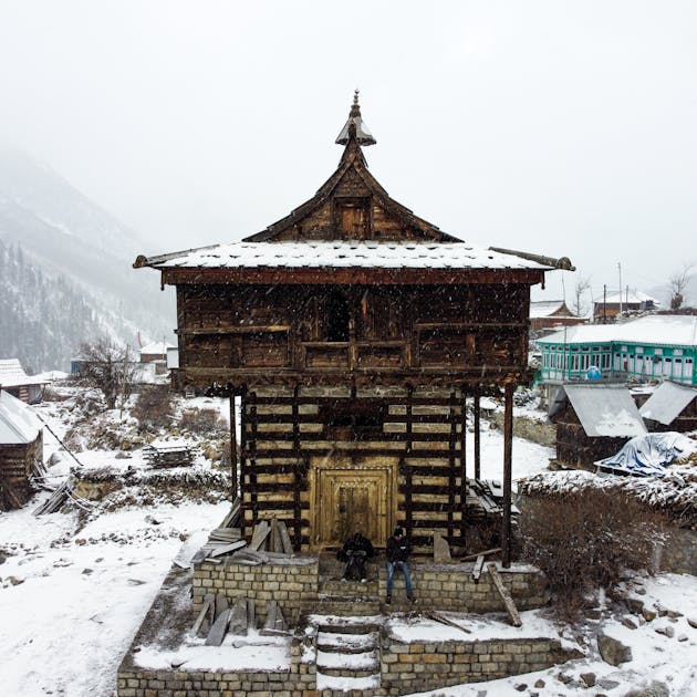 Traditional wooden temple in snowy landscape in the Himalayas, showcasing snowfall and rustic architecture.