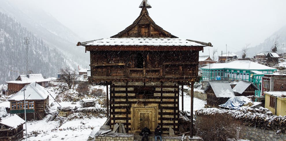 Traditional wooden temple in snowy landscape in the Himalayas, showcasing snowfall and rustic architecture.